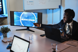 African man pointing at a monitor that is displaying the word blockchain